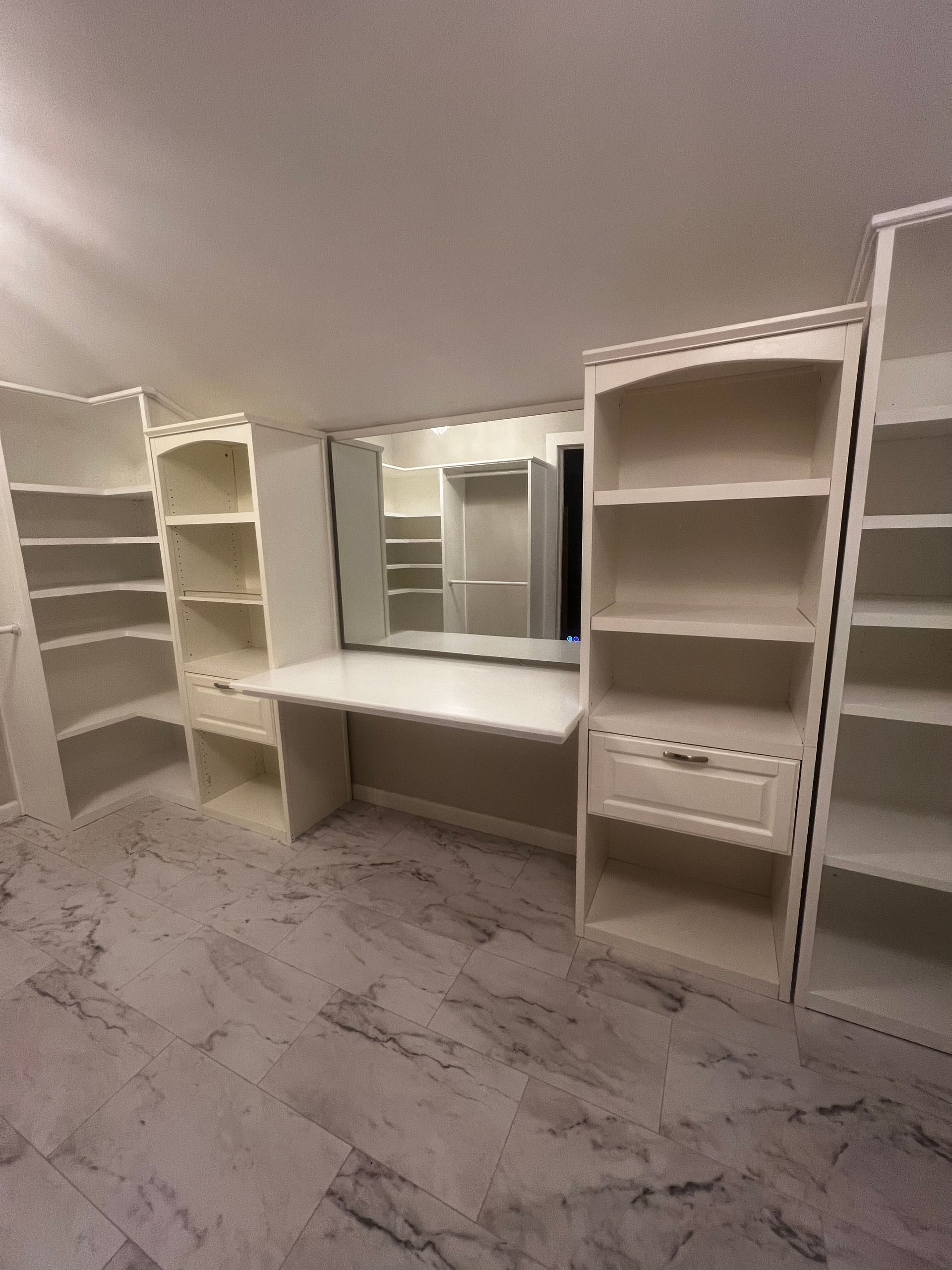 White built-in closet and vanity with shelves, drawers, and a mirror in an empty room with wood-look flooring.