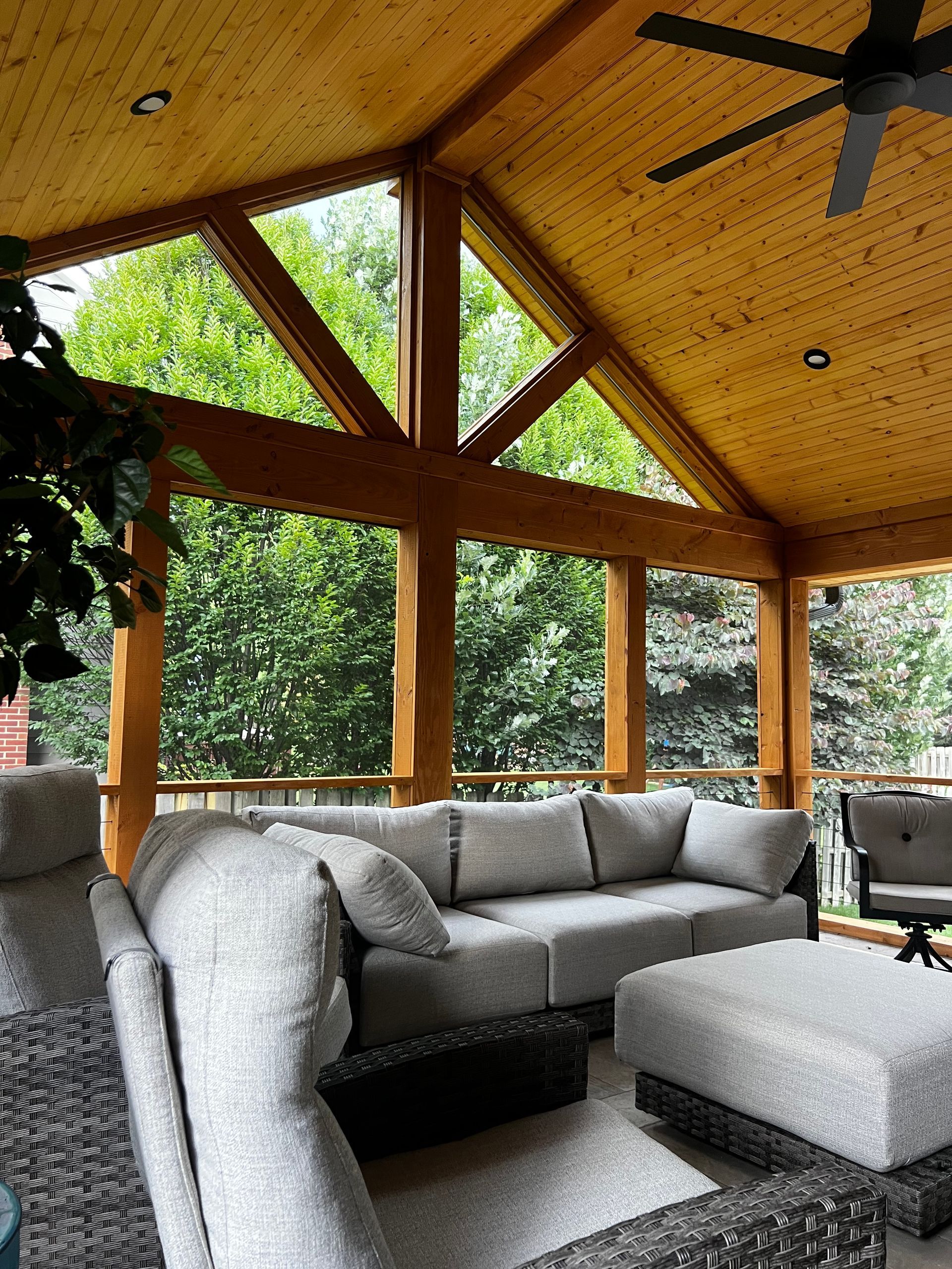 Covered outdoor patio with gray sectional sofa, ottoman, and wood ceiling under ceiling fan