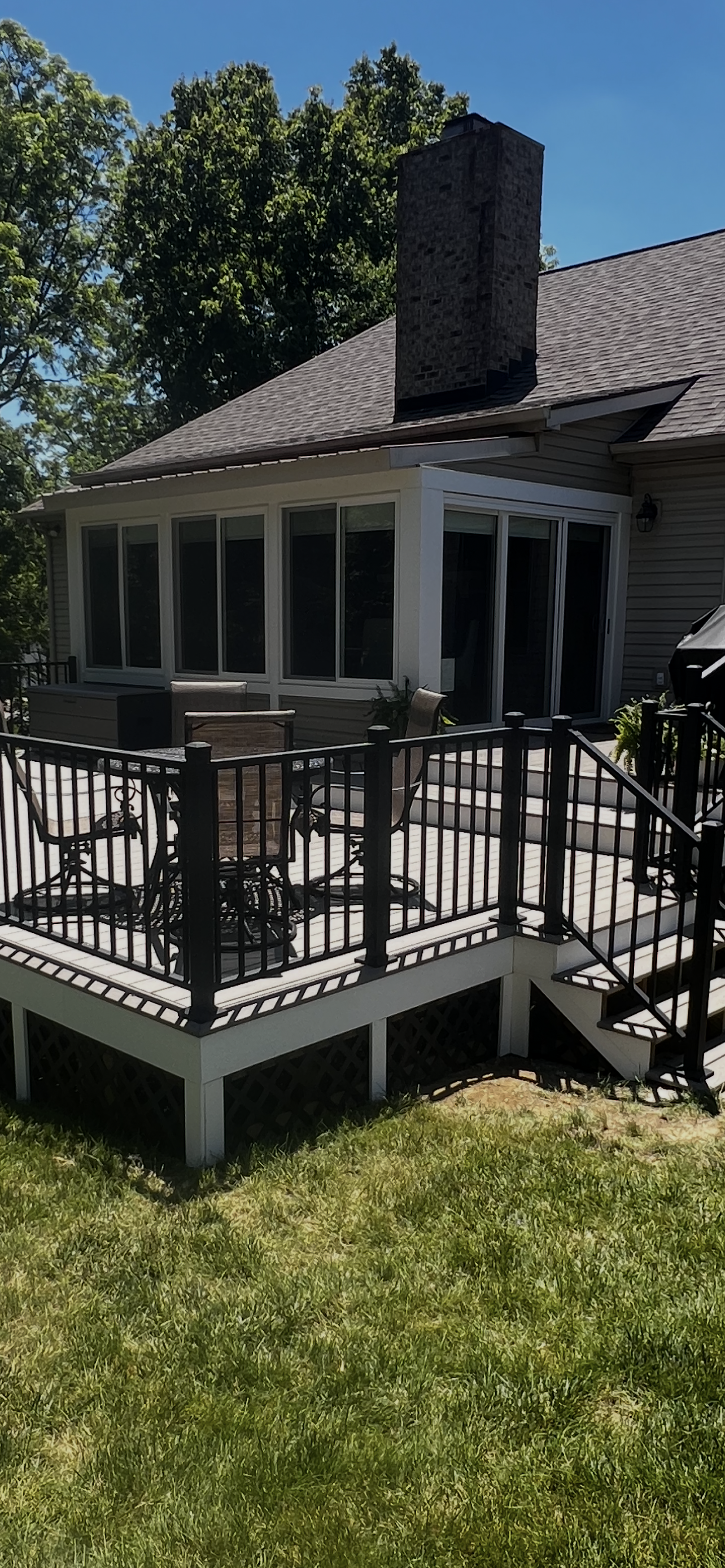 Brick house porch with black railing, screened windows, and a small front deck in sunlight