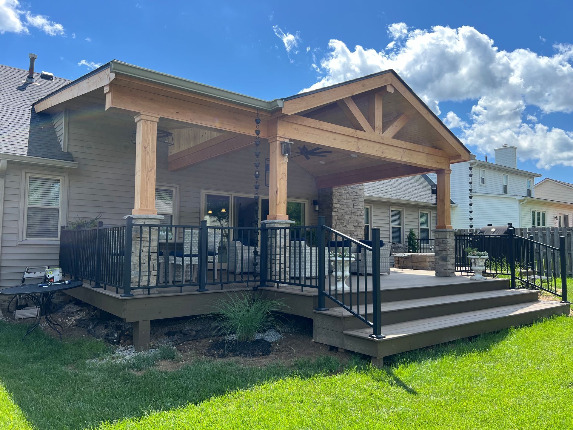 Covered wooden porch with black railings and steps on a house under a blue sky.