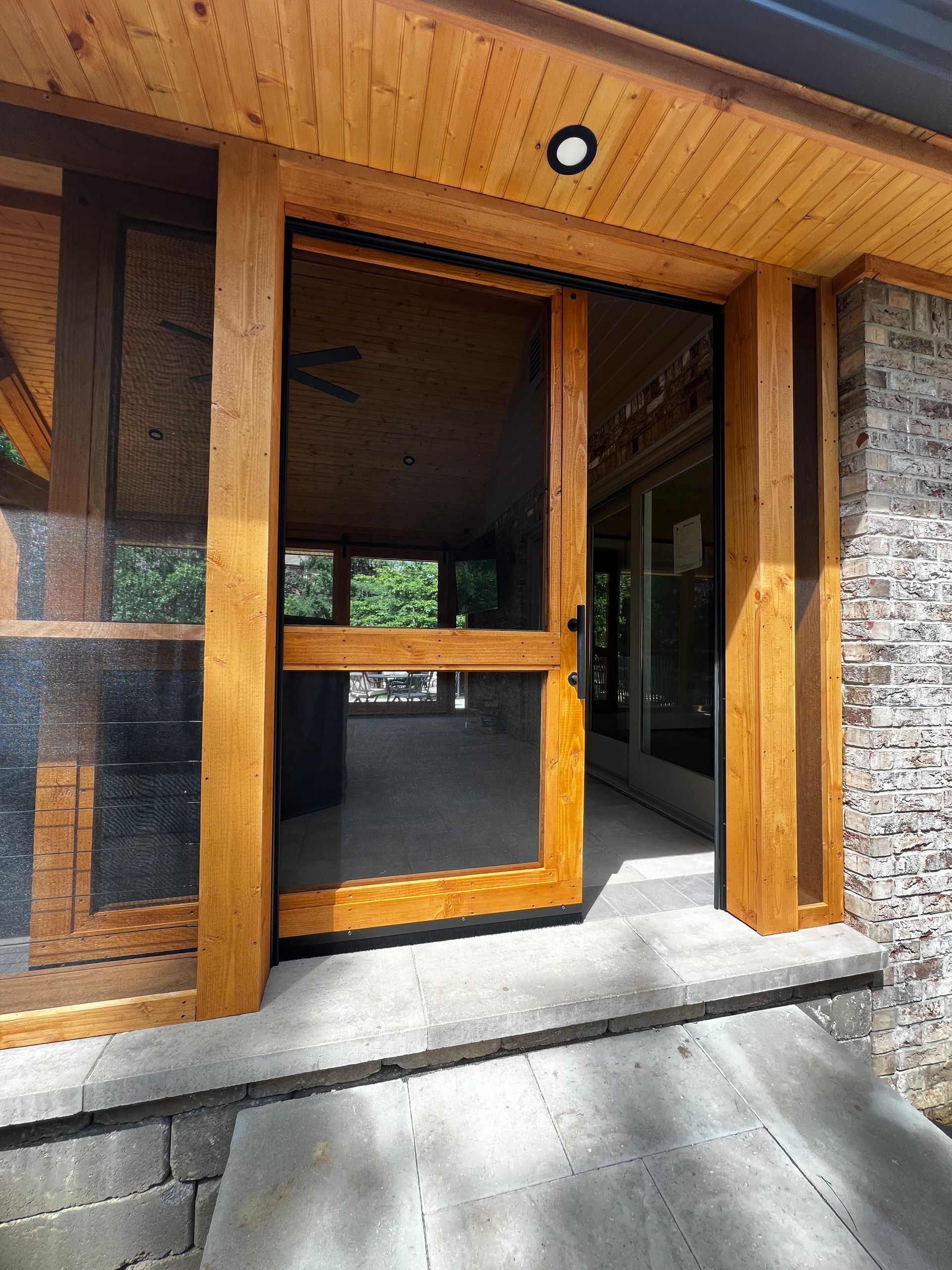 Wood-framed glass entrance door with sidelights and concrete steps under a wood-paneled overhang.