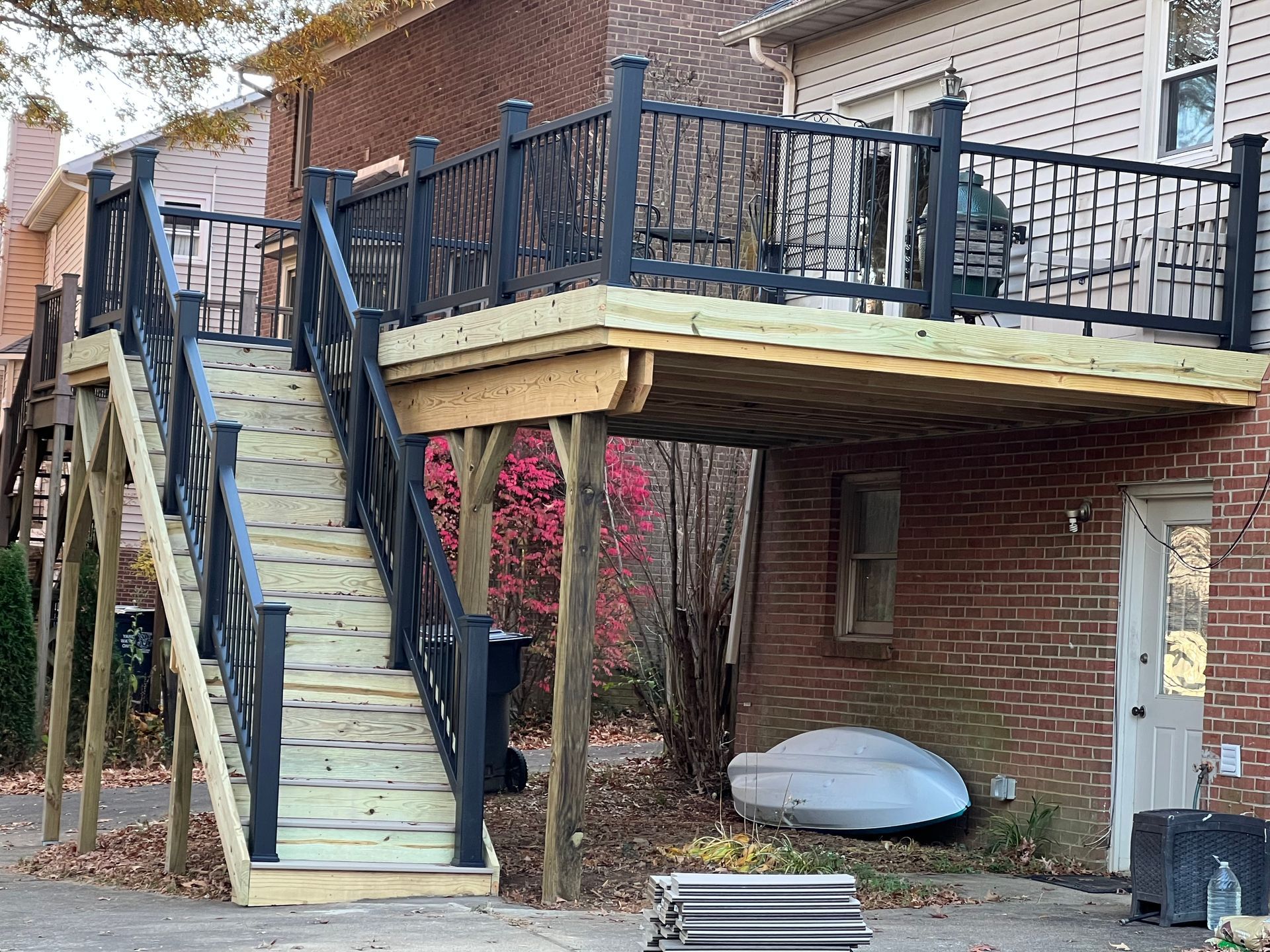 Exterior staircase leading to a wooden deck on a brick house, with black railings and a door below.