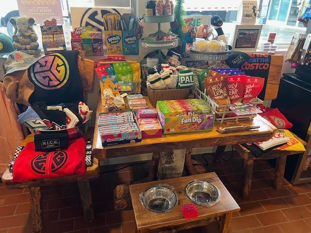 A table display inside a store featuring various snacks, merchandise with a circular logo, and a raised pet bowl stand.