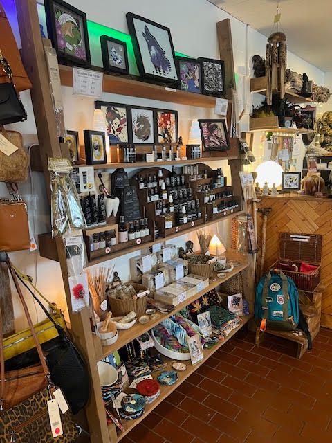 A wooden shelving unit in a shop filled with small bottles, art prints, bags, and miscellaneous gifts on display.