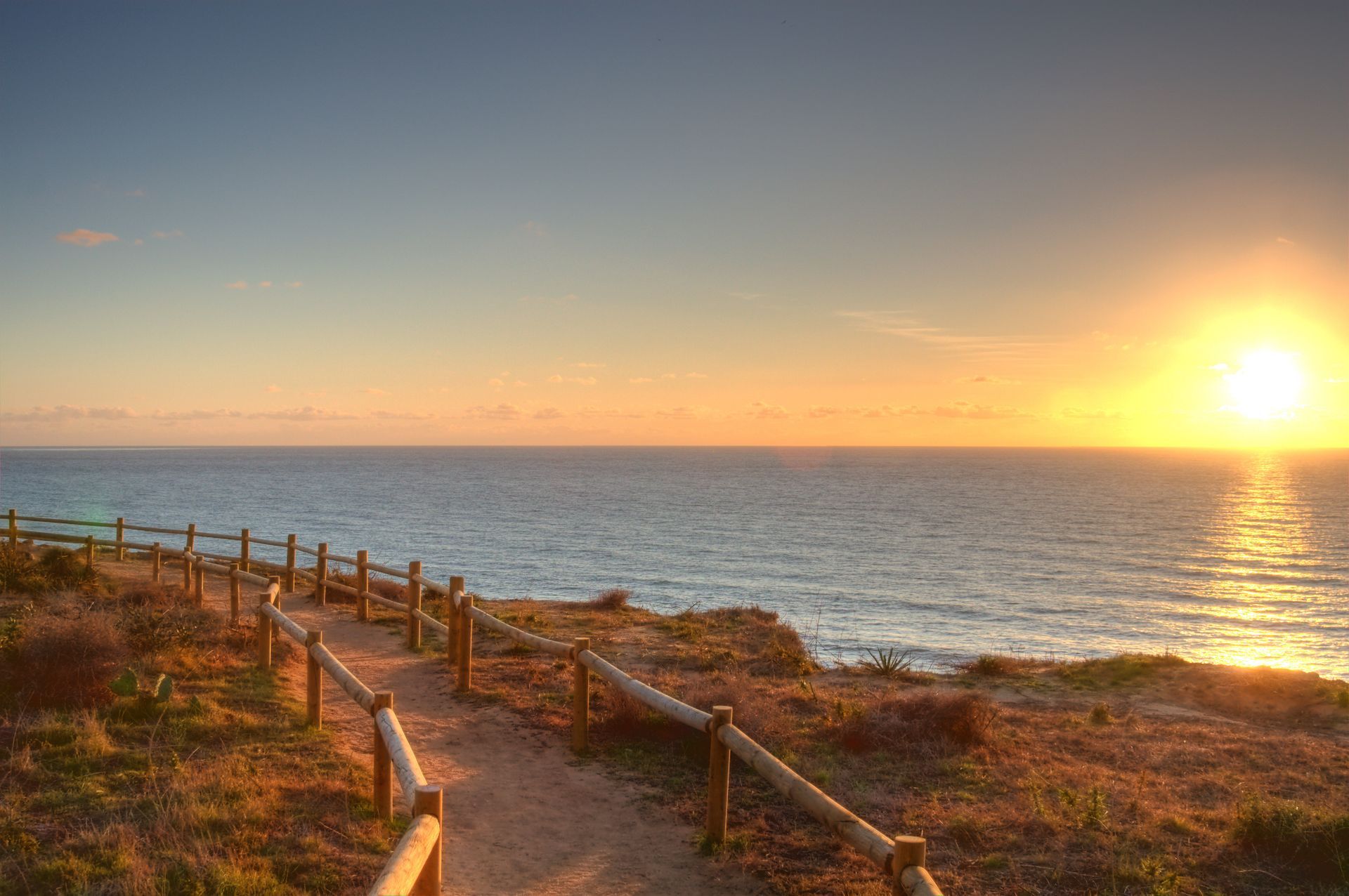 Sunset over the ocean with a wooden boardwalk and fence along a coastal path