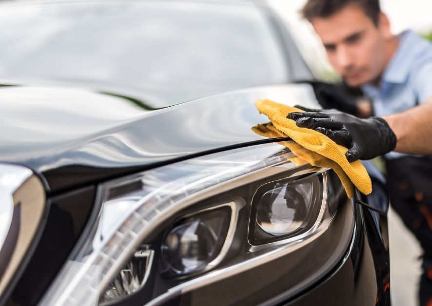 Man in gloves polishing a black car with a yellow cloth.