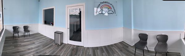 Empty waiting room with blue walls, gray wood floor, chairs, a TV, and a wall mirror in a bright hallway.