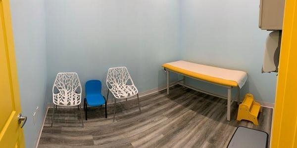 Small waiting room with two white chairs, a blue stool, a yellow bench, and a gray carpet floor.
