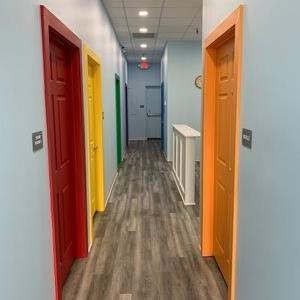 Narrow hallway with colorful doors and gray wood flooring in a building