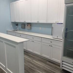 White kitchen with long cabinets, light blue backsplash, island, and gray wood-look flooring