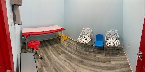 Small waiting room with red and white chairs, a blue stool, and a red-covered bench on gray wood flooring.