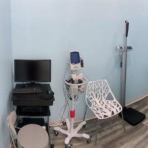 Medical room with exam equipment, computer monitor, chair, and standing scale against a light blue wall