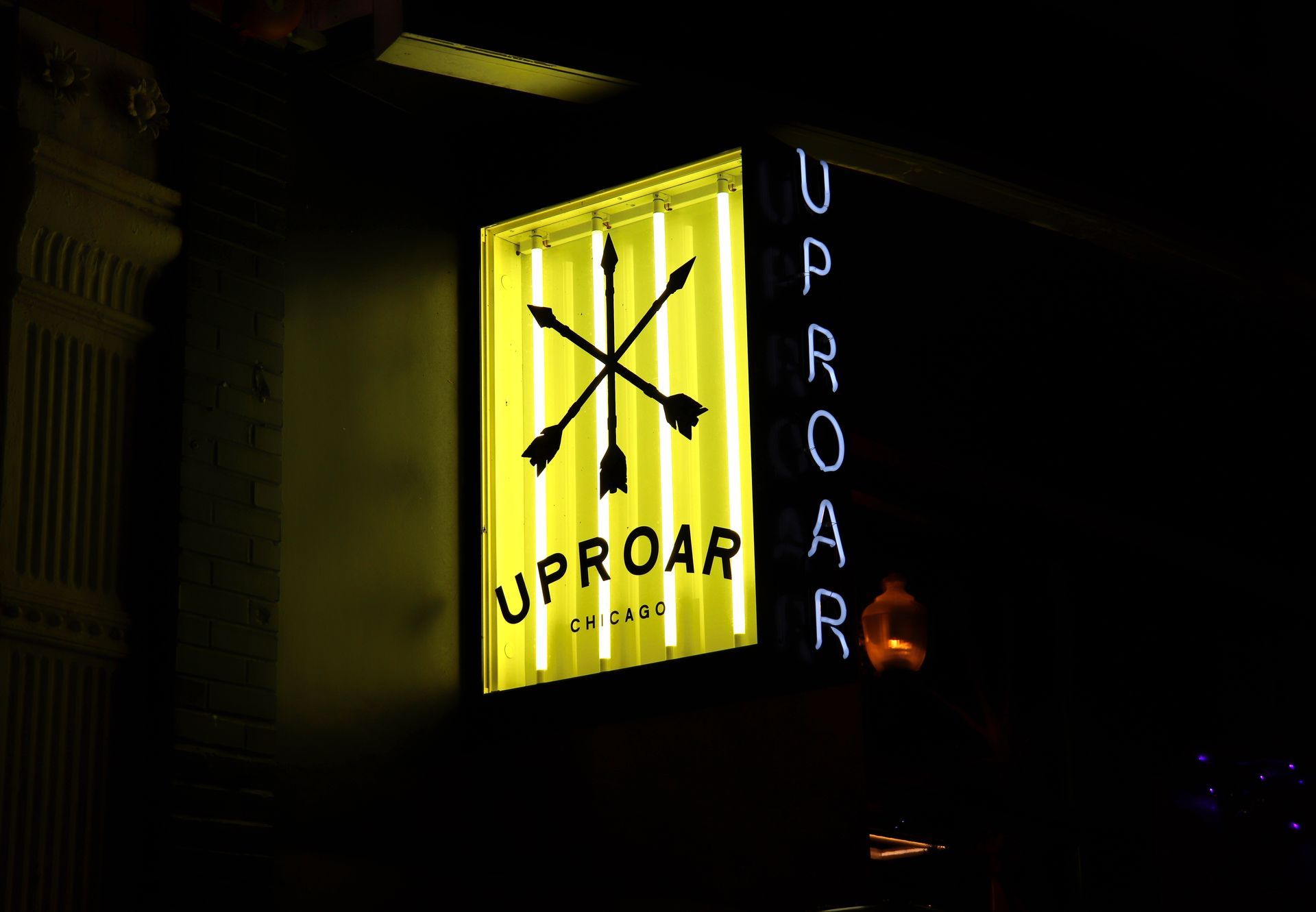 Sign for Uproar, a bar, in yellow and black with arrows; the neon sign has 