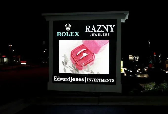 Sign at night: Rolex and Razny Jewelers logo, engagement ring in a pink box, and Edward Jones Investments.