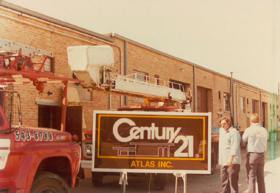 Century 21 Atlas Inc. sign with a truck, two men, and brick building.