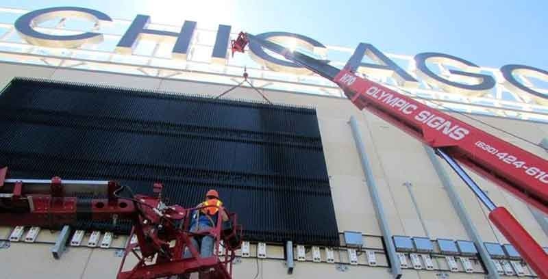 Workers in a cherry picker installing a dark panel on a building with
