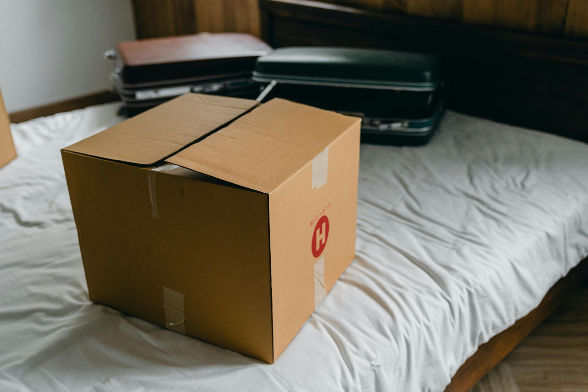 Packed and sealed moving boxes on bed w/ luggage, showing completed packing for professional movers