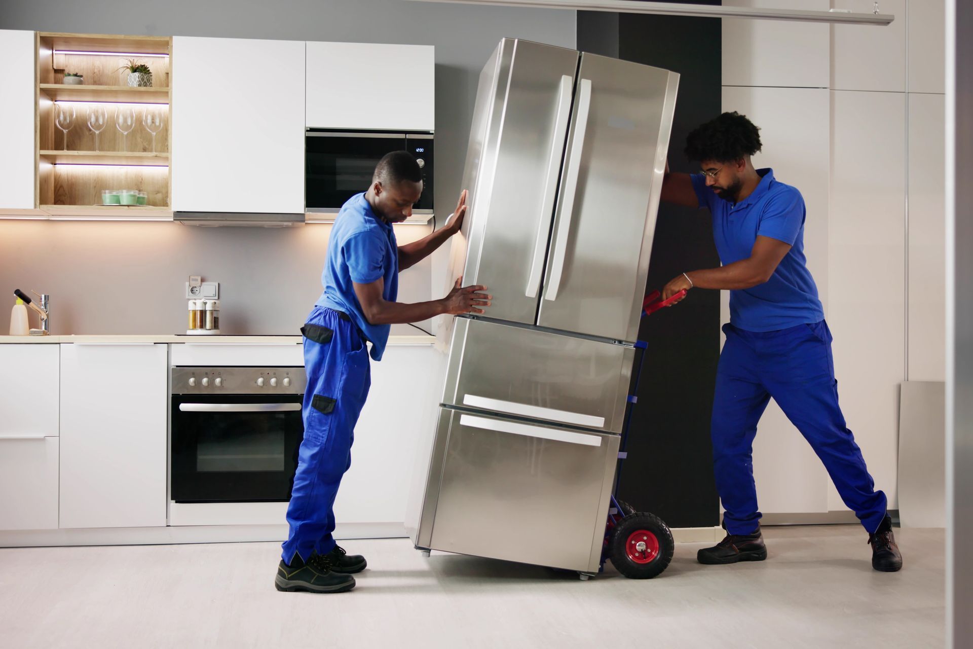 Two hiFive moving and hauling employee are carrying a refrigerator on a dolly in a kitchen