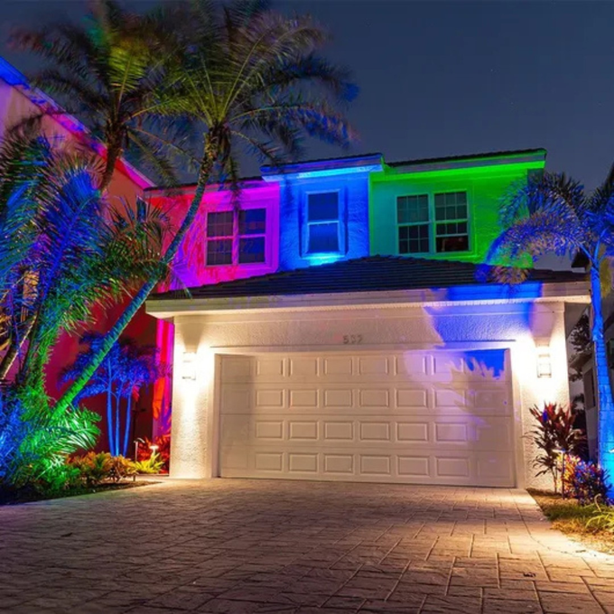 House exterior illuminated with colorful lights; palm trees and driveway.