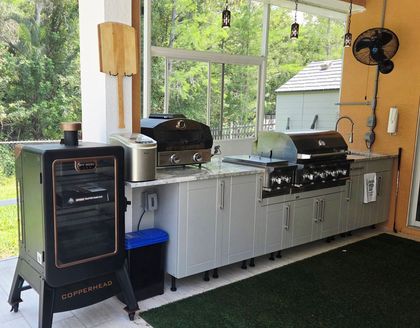 Outdoor kitchen with grill, cabinetry, and wooden pergola.