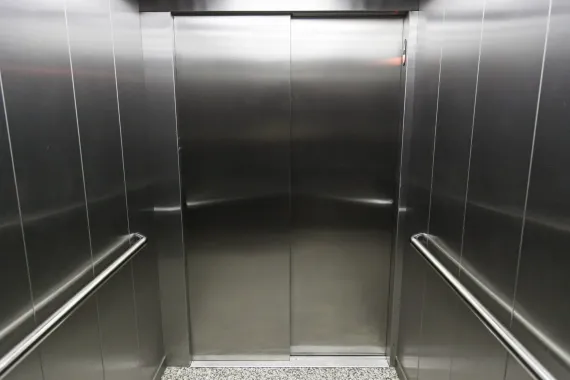 Interno vuoto dell'ascensore in acciaio inox con porte chiuse e corrimano su entrambi i lati.