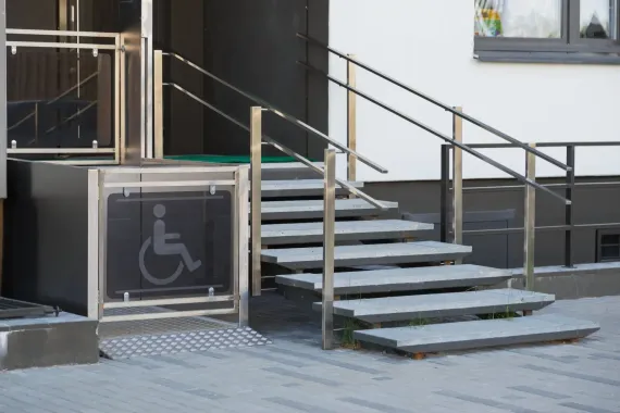 Rampa e scale accessibili accanto all'ingresso dell'edificio, con cartello per sedia a rotelle.