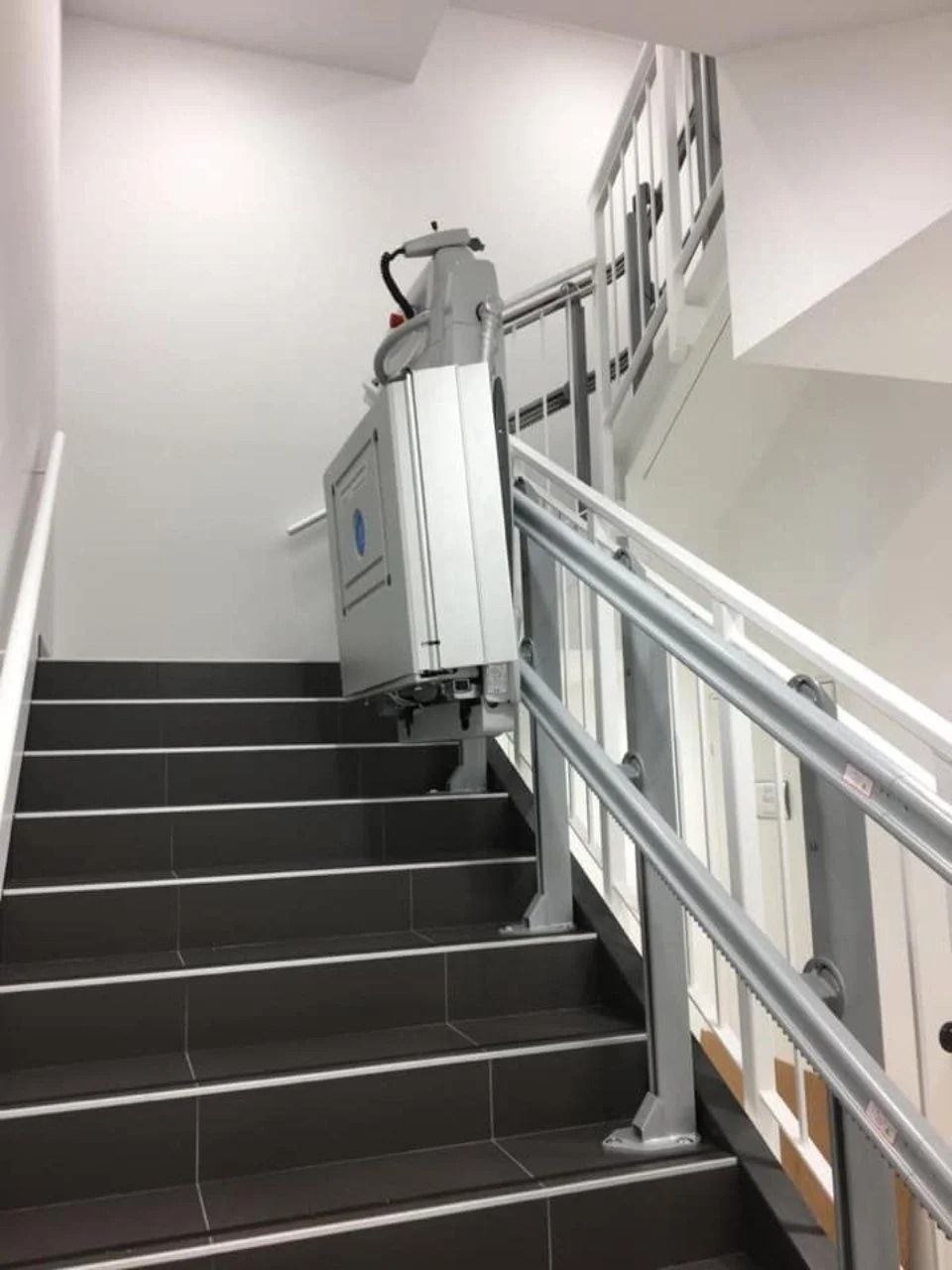 Vano scale con montascale su una scala rivestita di moquette scura e corrimano in metallo.
