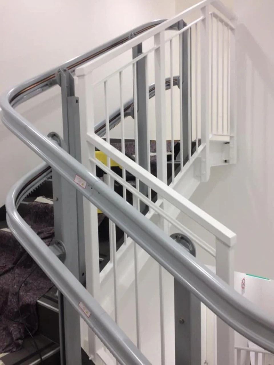 Scala curva con ringhiere bianche e gradini rivestiti di moquette grigia in un edificio moderno.