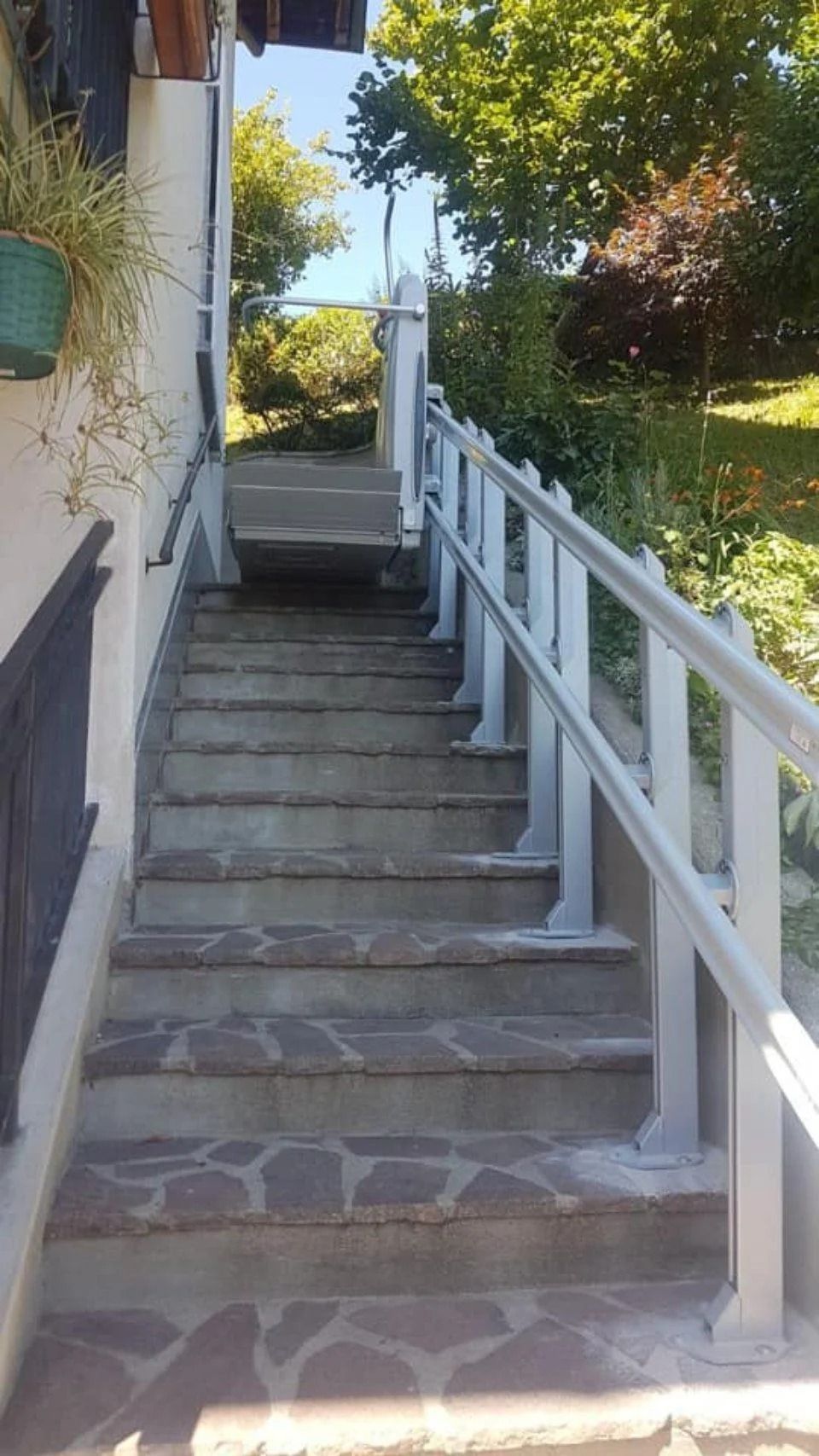 Scala in pietra con ringhiera bianca accanto a una casa, che conduce verso un sentiero soleggiato in giardino.