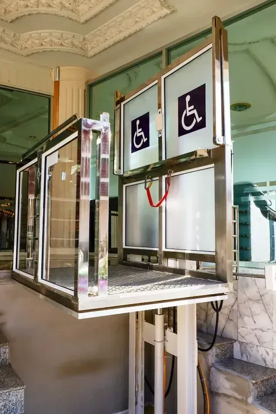 Piattaforma accessibile con simboli per sedia a rotelle e ascensore metallico all'ingresso dell'edificio.