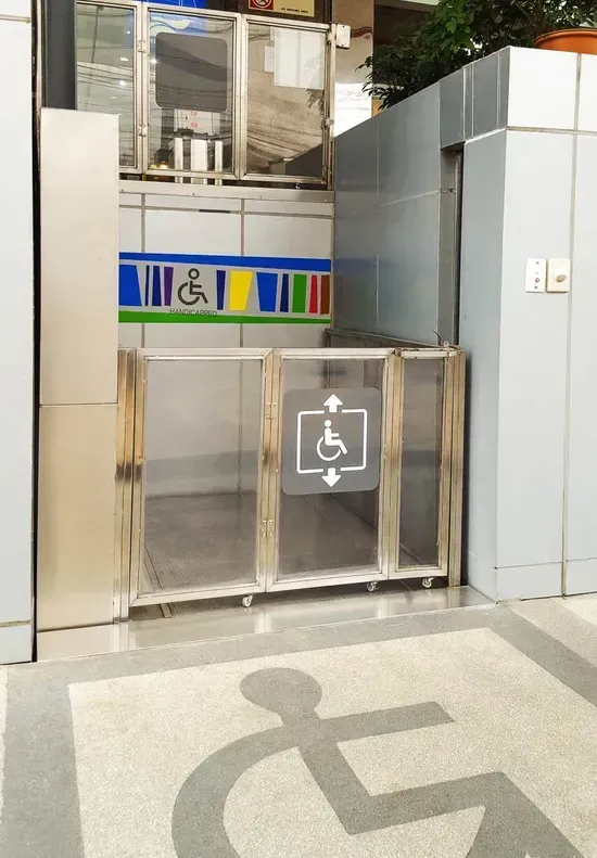 Ingresso accessibile all'edificio con cancello in metallo, cartello ascensore e simbolo della sedia a rotelle sul pavimento.