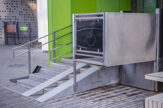 Rampa e scalini in metallo per sedie a rotelle che conducono all'ingresso di un edificio con una parete verde brillante.