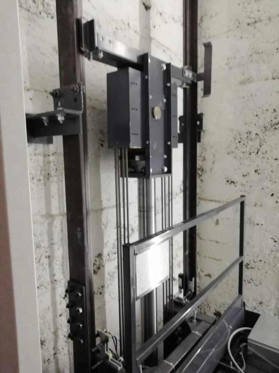 Meccanismo di ascensore industriale accanto a una ringhiera di vetro in una tromba delle scale in cemento.