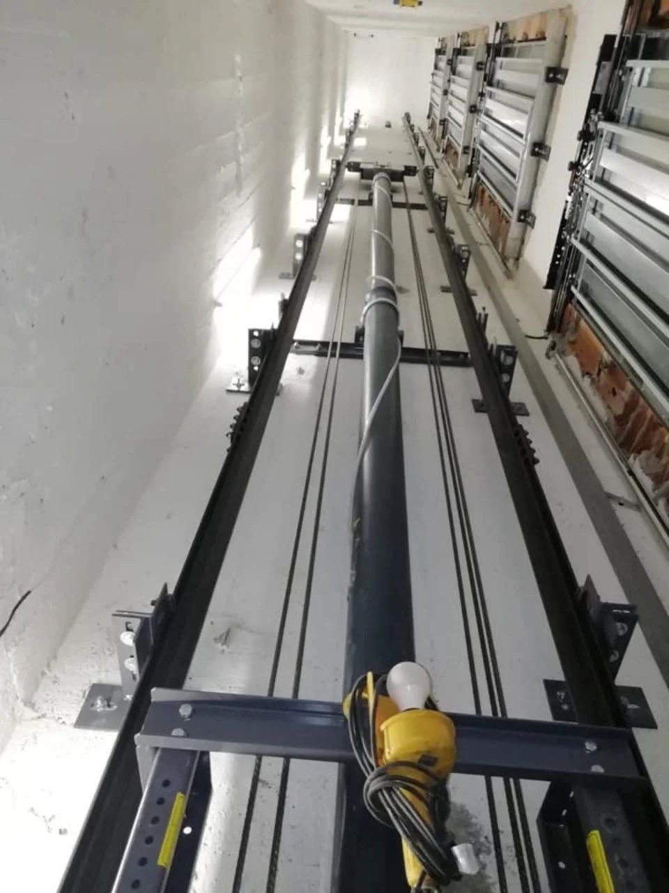 All'interno del vano di un edificio, un ascensore sospeso o un sistema di cavi scorre verticalmente lungo una parete bianca e un sistema di binari.