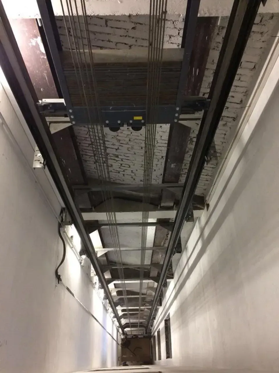 Lungo corridoio industriale con soffitto a vista, tubature e pareti bianche che si perdono in lontananza