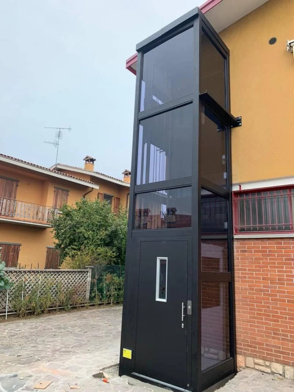 Alto ascensore esterno nero accanto a un edificio in mattoni in un cortile residenziale