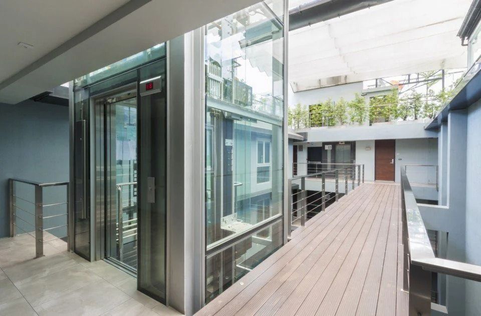 Una moderna passerella in vetro collega gli edifici del cortile con una pavimentazione in legno e una ringhiera in metallo.