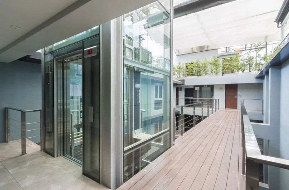 Una moderna passerella in vetro collega gli edifici del cortile con una pavimentazione in legno e una ringhiera in metallo.