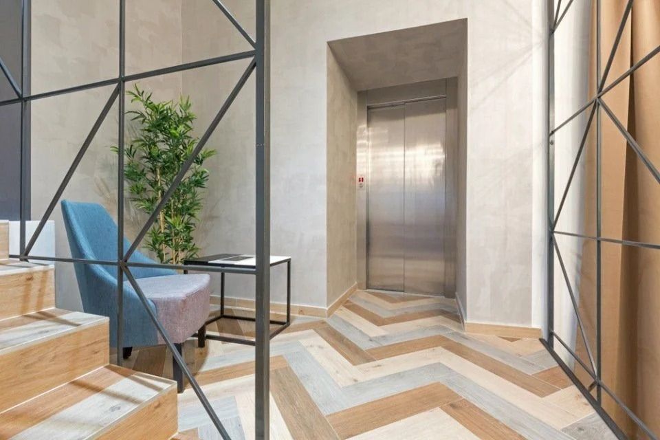 Atrio moderno con ascensore, scale in legno, poltrona blu e decorazioni geometriche alle pareti.