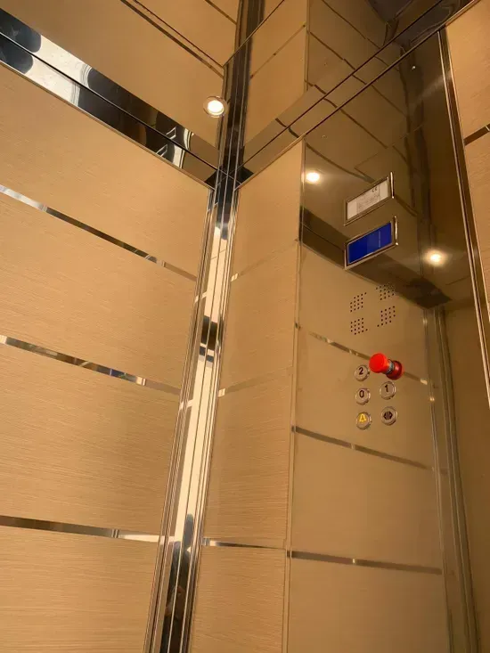 Interni moderni dell'ascensore con porte a specchio, pareti beige e pannello di controllo con pulsante di emergenza rosso.