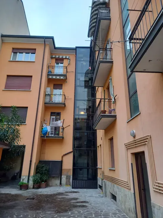 Stretto cortile tra palazzine di appartamenti color pesca con balconi e un cancello nero.