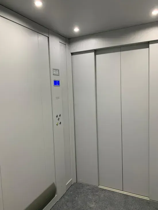 Ascensore moderno vuoto con porte bianche, pareti grigie e pannello di controllo blu.