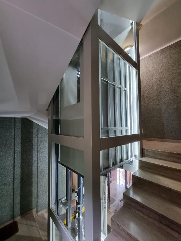 Vano ascensore in vetro tra le scale all'interno di un edificio, con scale e ringhiere metalliche.