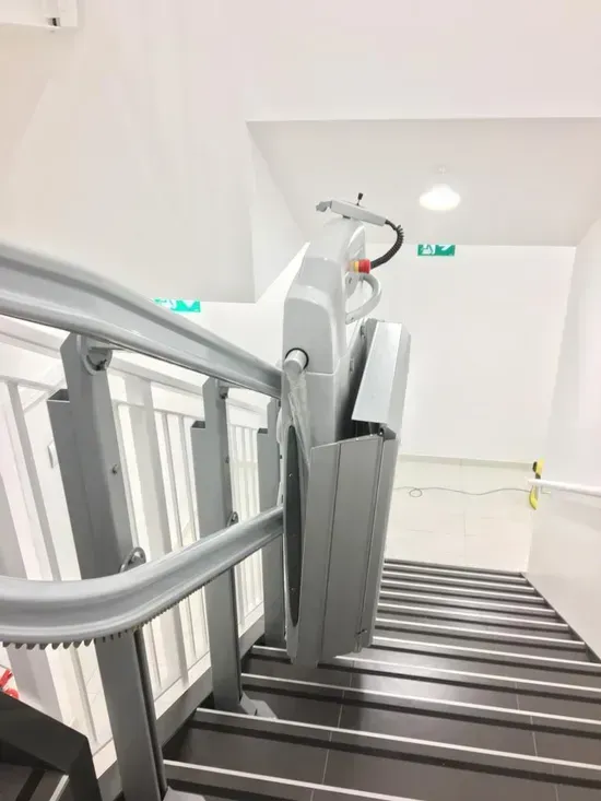 Scala interna con ringhiere grigie e montascale centrale in un corridoio bianco.