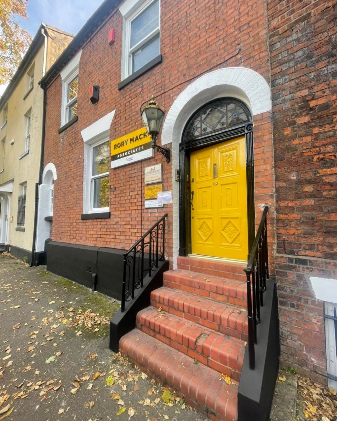 Brick building with bright yellow arched door, red steps, and a black railing on a wet street.