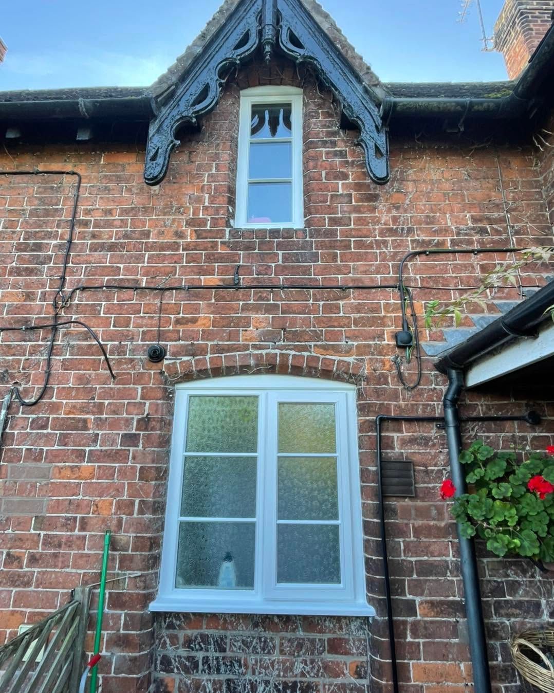 Brick house wall with white-framed windows and ornate dark trim under the roofline