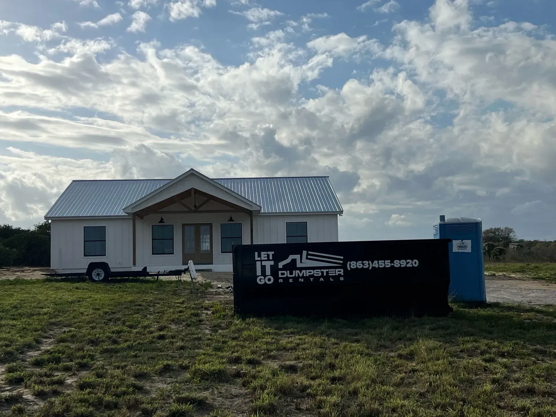 House under construction with a large black dumpster in front under a cloudy sky