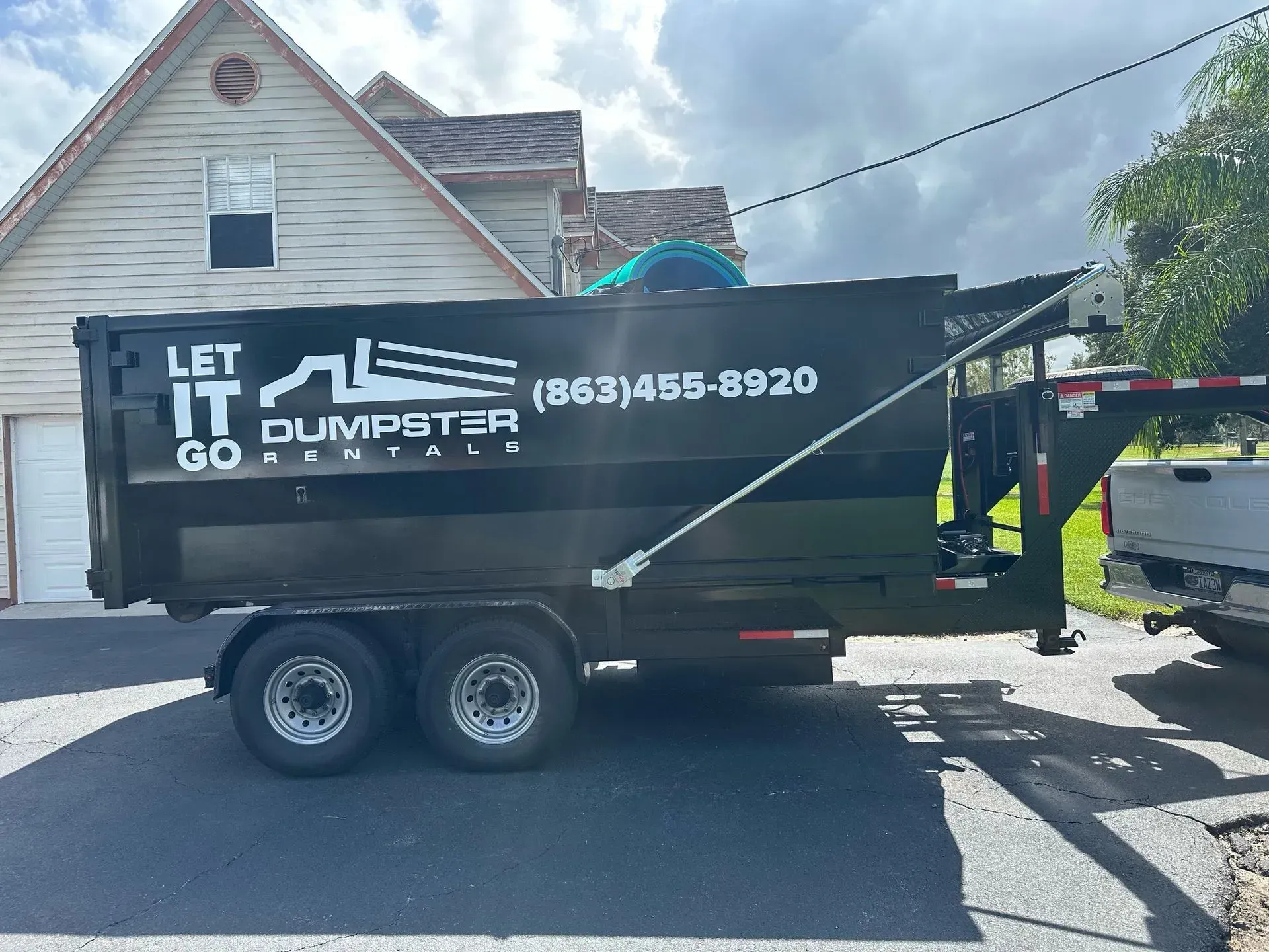 Black dumpster trailer with “Let it go” logo parked on a street in front of a house
