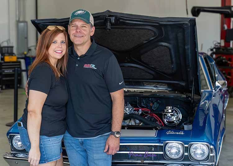 The owners of Auto DR smile while standing in front of a vintage car from Richmond.