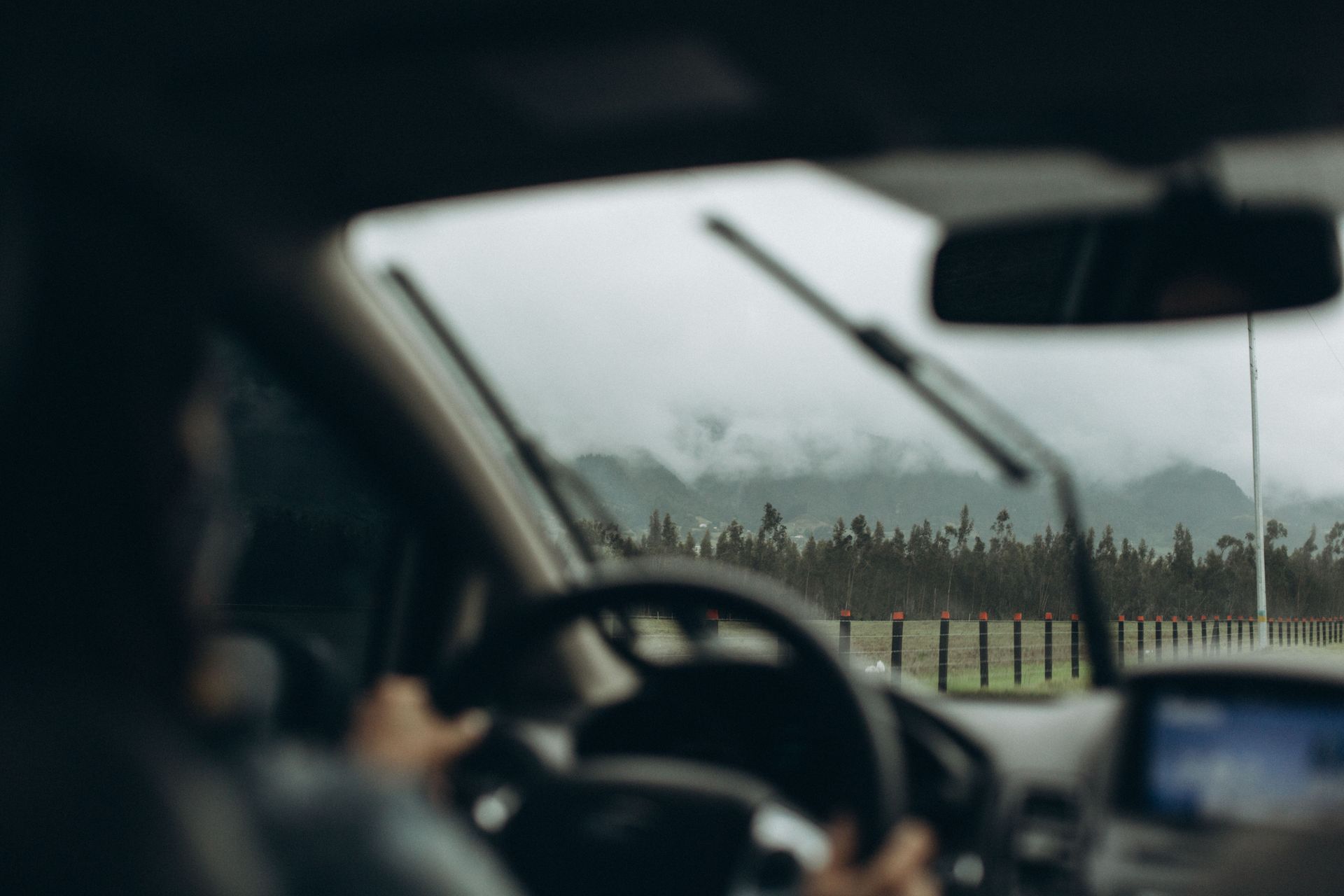 Driver’s view through a rainy windshield on a highway, with dashboard and rearview mirror visible